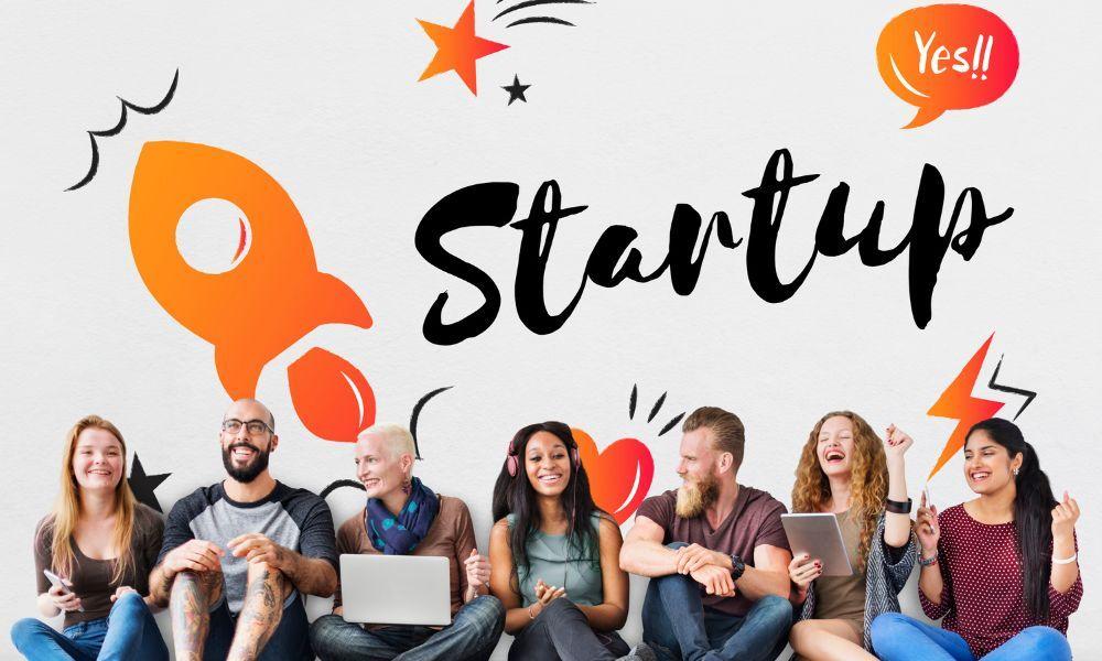 Diverse group of young entrepreneurs sitting together with laptops and tablets, with the word "Startup" and a rocket illustration in the background